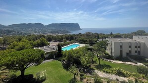 Ein Pool, umgeben von Grünflächen und Gebäuden, mit Blick auf das Meer und die fernen Hügel.