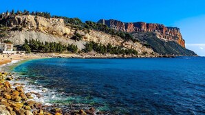 Eine Küstenlandschaft mit felsigem Strand, klarem, blauem Wasser und einer markanten Klippe mit Ruinen.