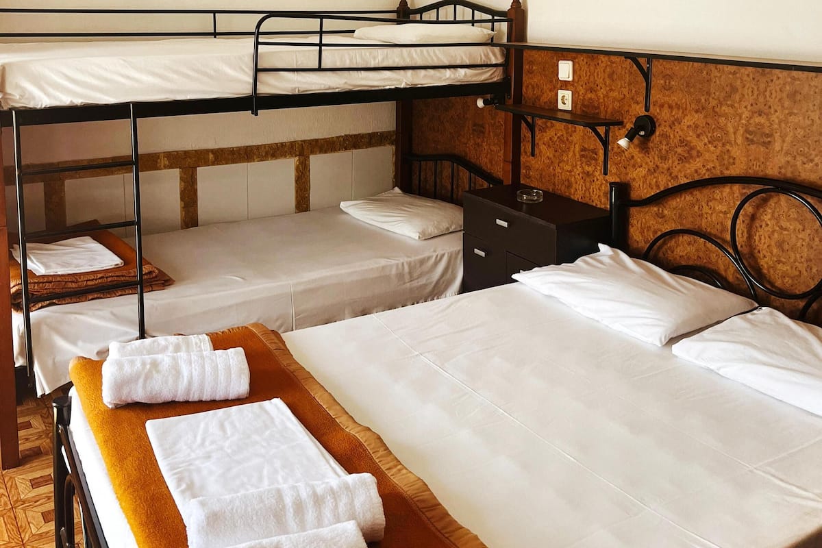 A dormitory room with bunk beds, a wooden headboard, a tapestry, and a framed picture on the wall.