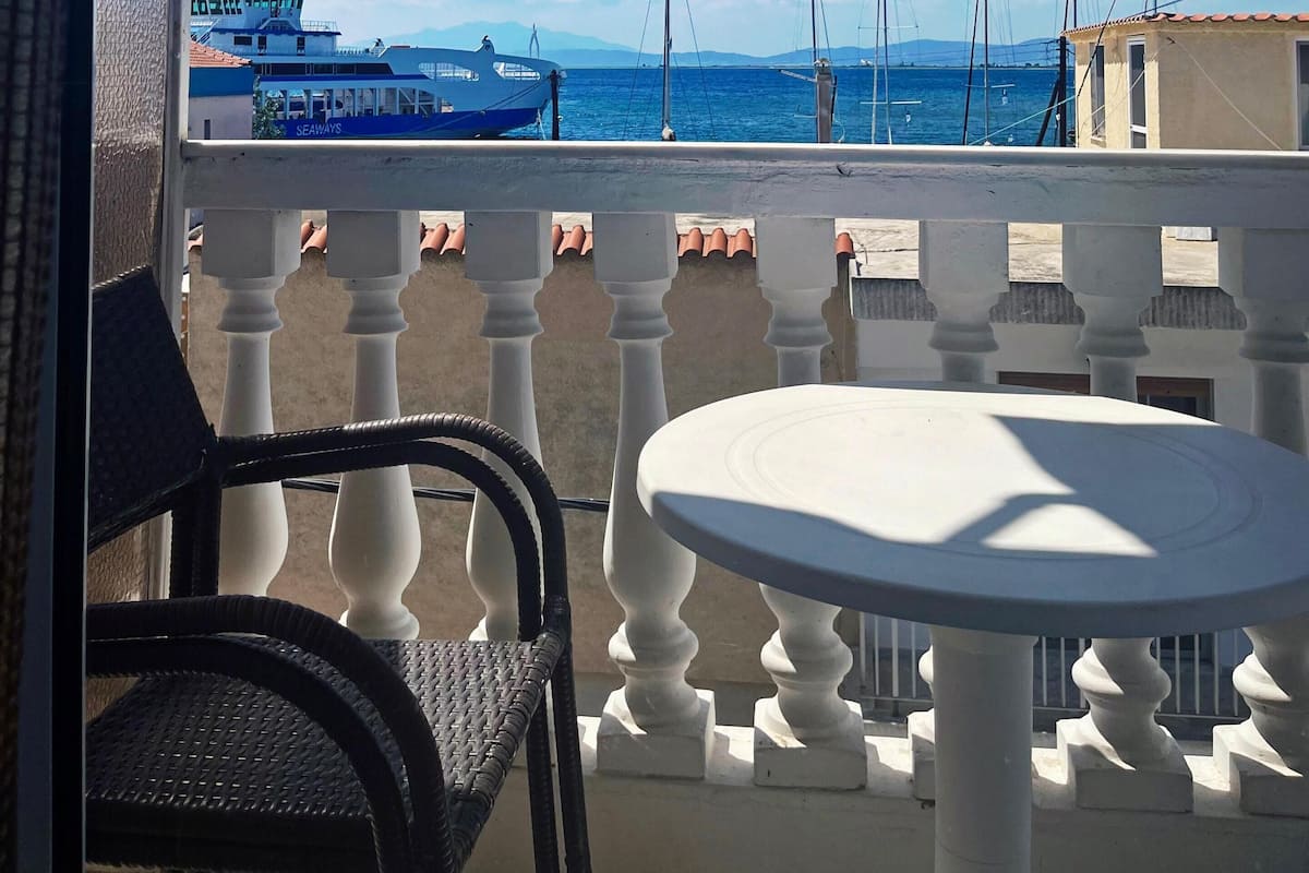 A balcony with a white balustrade, a round table, and a view of the sea with boats.