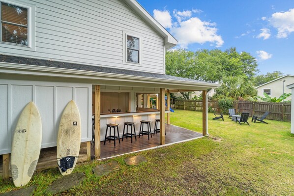 A house with a covered patio area, a small bar with stools, and two surfboards leaning against the house. - BEST Location on the Beach (Kill Devil Hills)