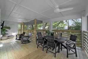 A covered outdoor patio with a wooden deck, a table with chairs, and a ceiling fan. - BEST Location on the Beach (Kill Devil Hills)