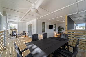 A spacious indoor area with a long table and chairs, wooden flooring, and a ceiling fan. - BEST Location on the Beach (Kill Devil Hills)