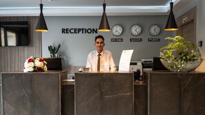 A reception desk with a modern design, featuring a nameplate, a clock, and a wall clock displaying times for New York, Algiers, and Paris. - Les Deux B Salsabil (Algiers)