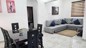 Ein Essbereich mit einem schwarzen Tisch und Stühlen, einem grauen Sofa mit gemusterten Kissen sowie Kunstwerken an den Wänden.