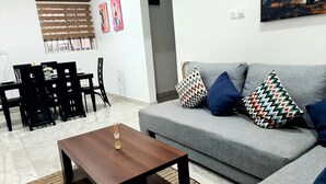 Ein Wohnzimmer mit grauem Sofa, gemusterten Kissen, einem Holztisch und einem Essbereich mit Stühlen und Tisch.