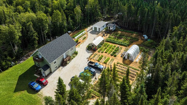 Ein Anwesen auf dem Land mit einem großen Haus, einem Gewächshaus und einem Gemüsegarten.