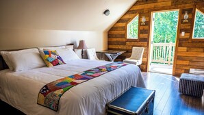 Ein Schlafzimmer mit einem großen Bett, einer Steudecke, einem Schreibtisch, einem Stuhl und Blick ins Freie.