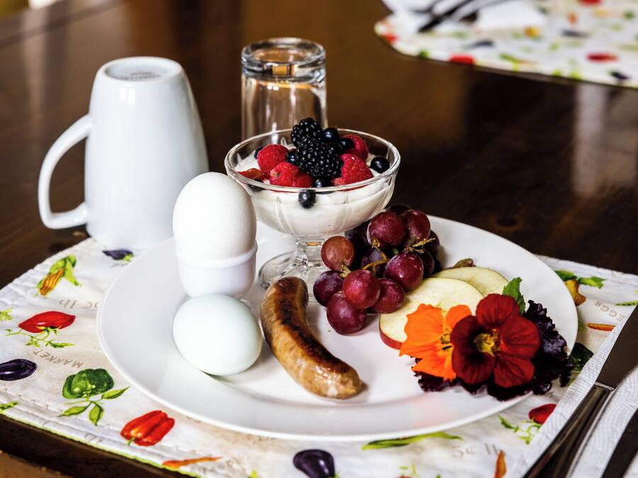 A breakfast plate with eggs, sausage, grapes, berries, and a flower.
