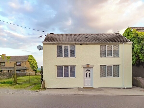 A two-story house with a white exterior, a tiled roof, and a front door. - 3 bedroom accommodation in Bridgend (Bridgend)