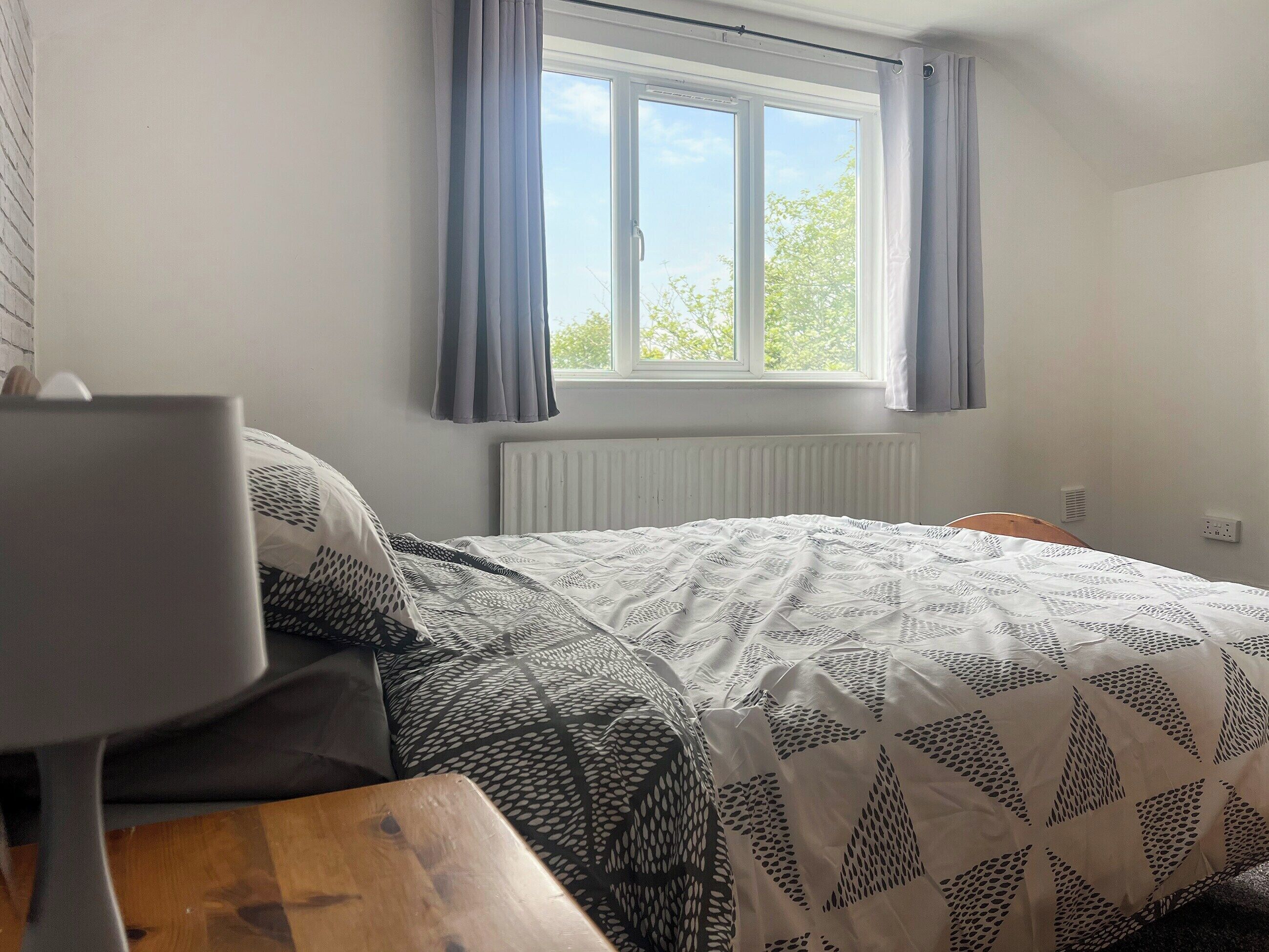 A bedroom with a bed, a wooden table, and a window with curtains.