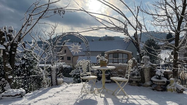 A snow-covered garden with a fountain, a small table, and chairs. - Beas Ferienglück (Busenberg)