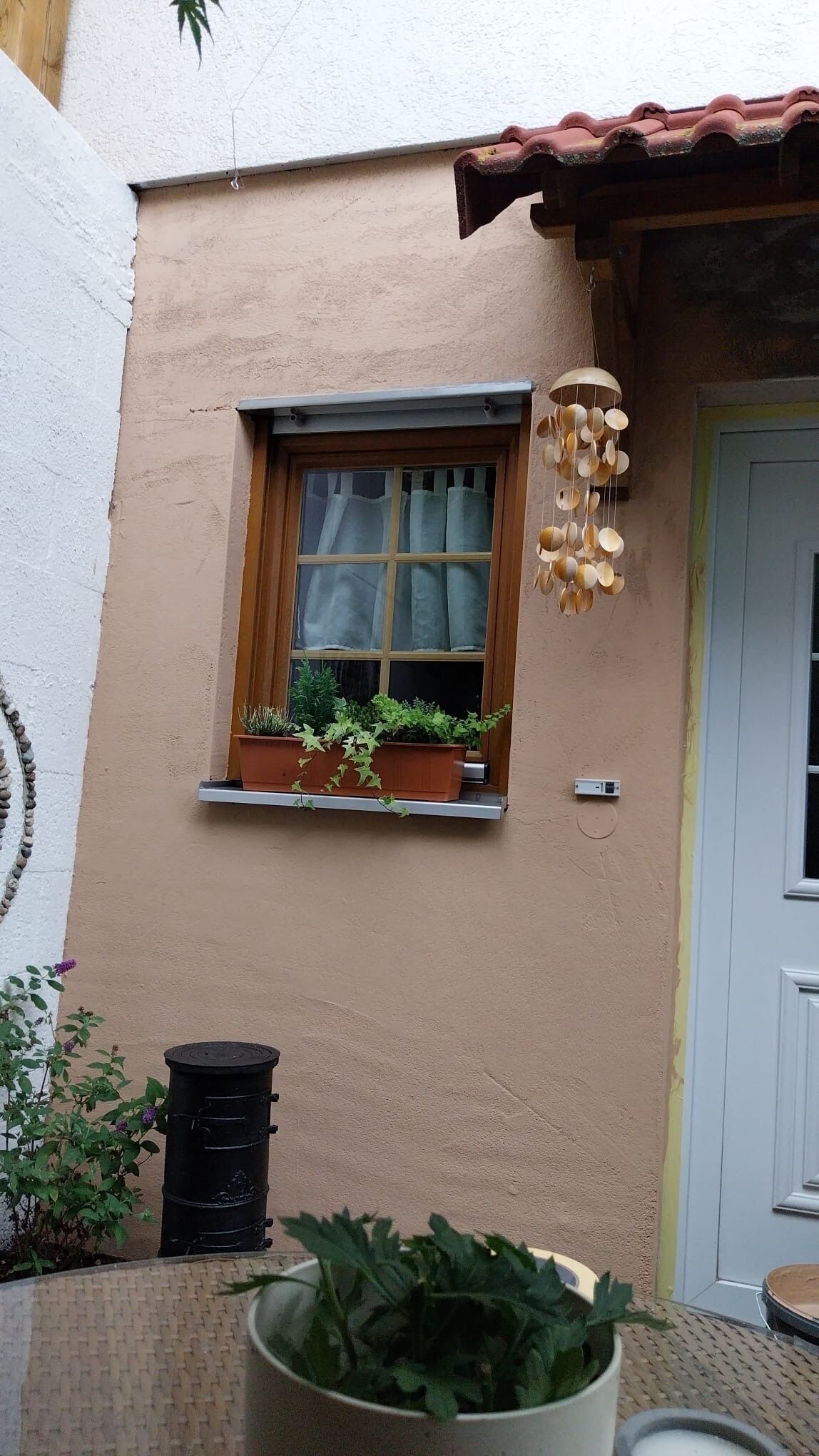 A building with a window with a curtain, a hanging wind chime, and a door.