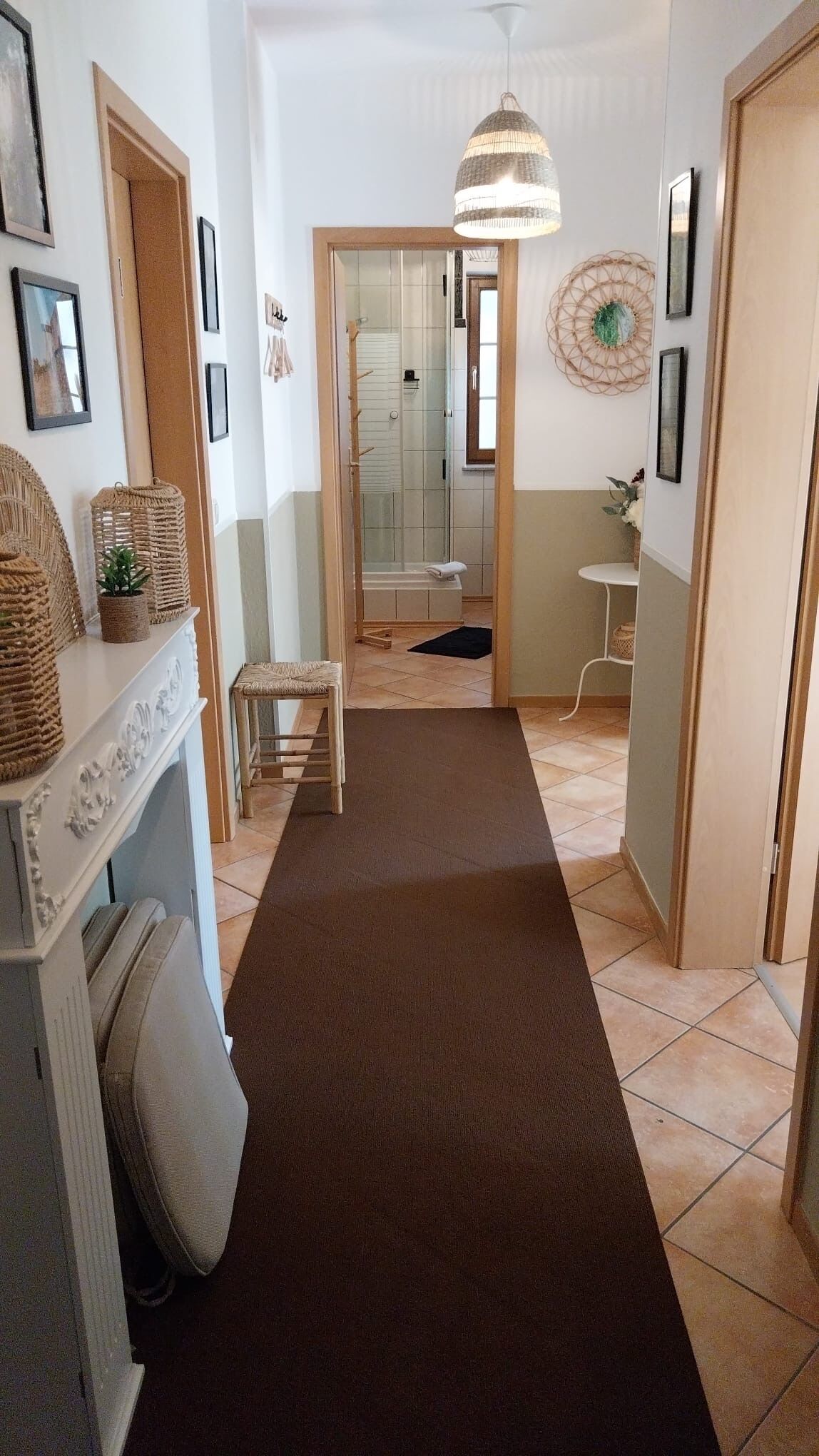 A hallway with a brown carpet, a wooden bench, a small table with a plant, and a hanging light fixture.