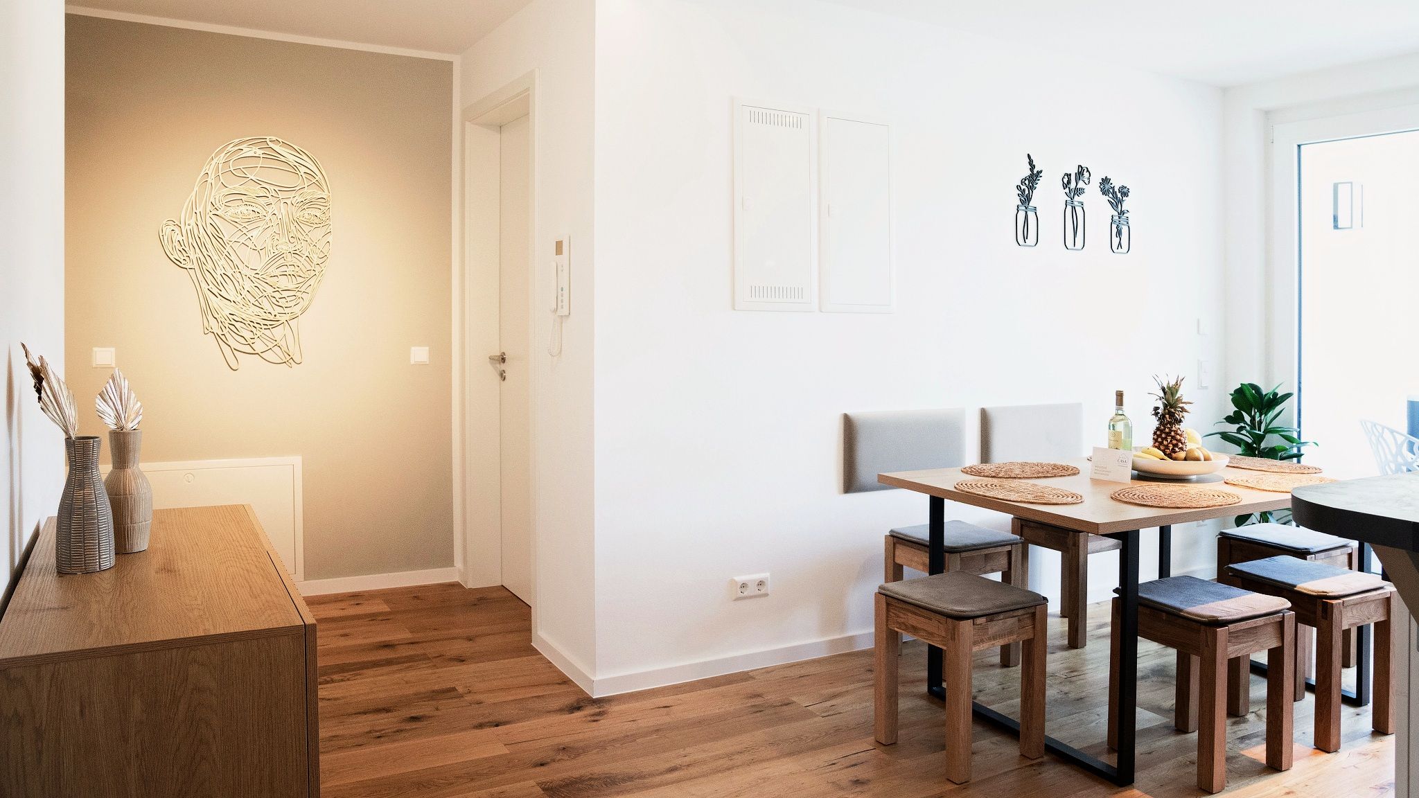 A modern dining area with a wooden table, chairs, and a wall-mounted light fixture.