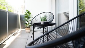 Un balcone con una sedia nera, un tavolino e una pianta in vaso.