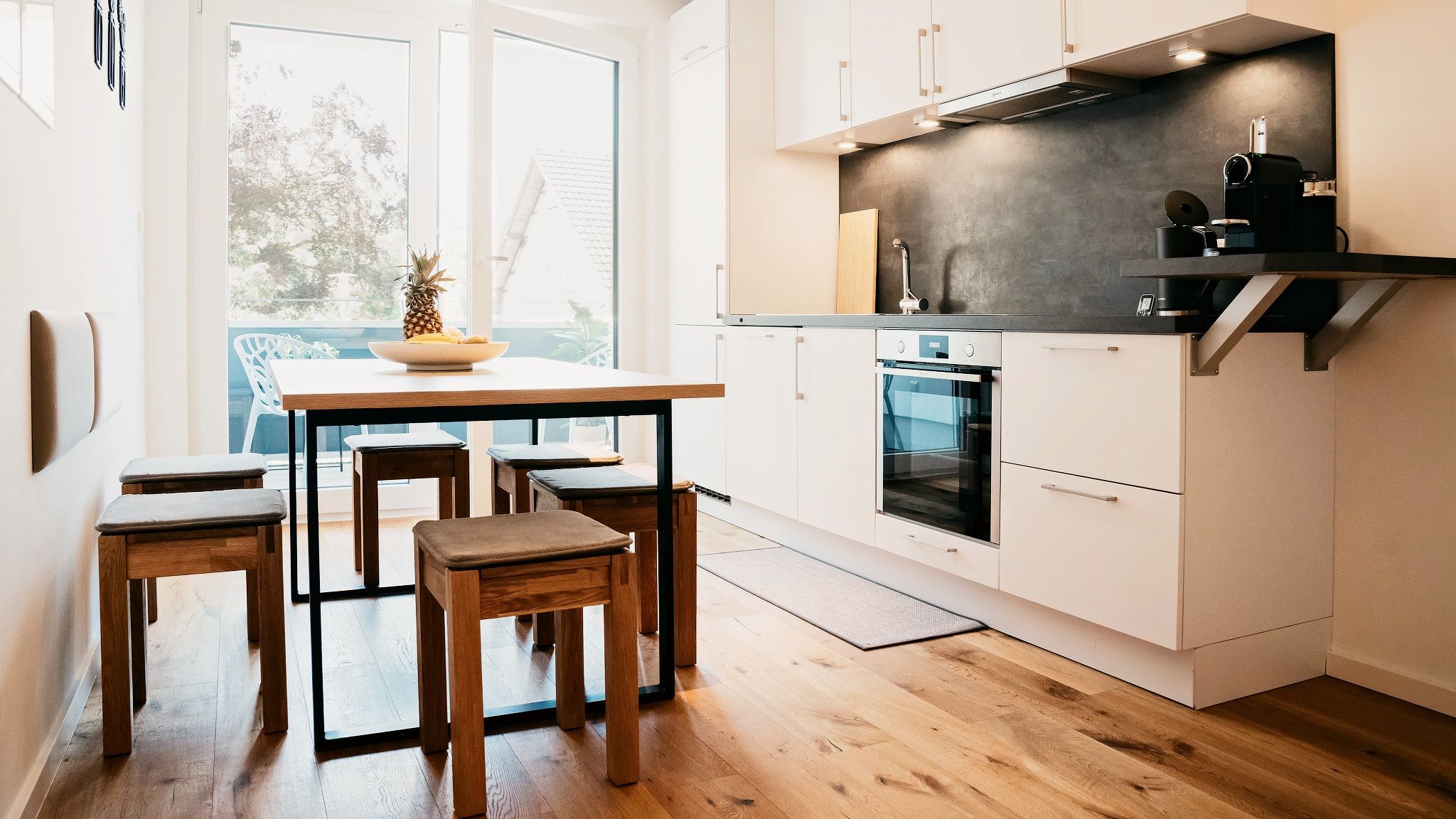 Una cocina compacta con armarios blancos, horno integrado y cafetera.