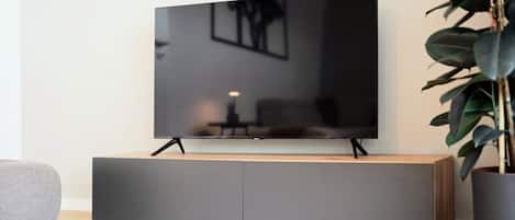 A flat-screen TV on a wooden cabinet with a plant beside it.