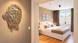 Une chambre moderne avec un grand lit, une table de chevet, une œuvre d’art abstraite accrochée au mur et une fenêtre avec des rideaux.