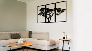 A living room with a sofa, a coffee table, a side table, and a wall-mounted artwork of a tree. - LaMiaCasa Tübingen | 2 Balconies | Private Parking | Central (Tübingen)