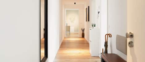 Un pasillo con suelo de madera, un banco, una puerta con perchero y una planta en la pared.