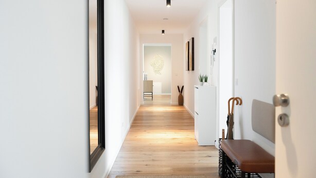 Un corridoio con pavimento in legno, una panca, uno specchio fissato al muro e una porta che dà su un'altra stanza.
