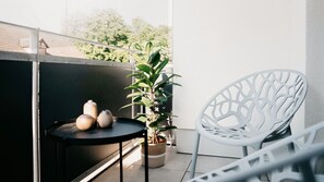Ein Balkon mit einem Blumentopf, einem weißen Stuhl und zwei Vasen auf einem kleinen runden Tisch.