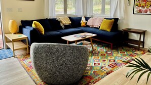 Ein gemütliches Wohnzimmer mit einem dunkelblauen Sofa, einem gemusterten Sessel und einem farbenfrohen Teppich.