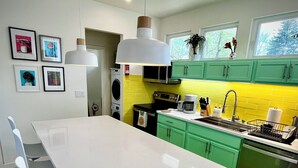 Eine moderne Küche mit einem weißen Tisch und Stühlen, grünen Schränken und einer gelben Spritzschutzwand.