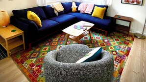 Ein Wohnzimmer mit einem blauen Sofa, einem kleinen Couchtisch und einem farbenfrohen Teppich.