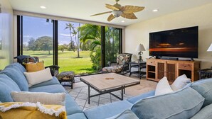 A living room with a sofa, coffee table, TV, and a ceiling fan.