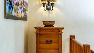 Une commode en bois sur laquelle est posé un bol, une lampe fixée au mur et un tableau accroché au mur.
