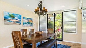 A dining area with a wooden table, chairs, a bench, a chandelier, and two paintings on the wall.