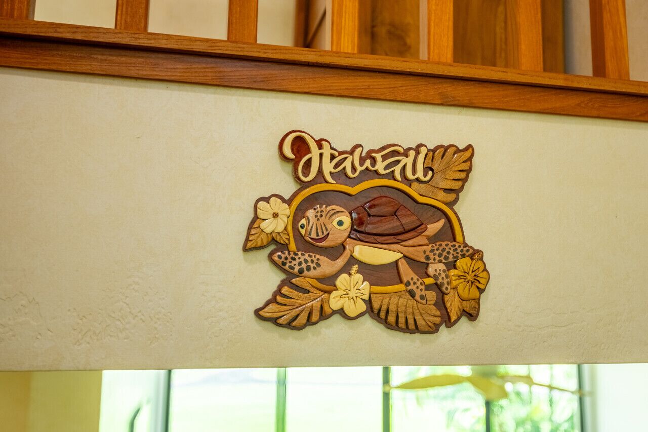 Een houten decoratie met de tekst 'Hawaii' en een schildpad, omringd door bloemen.