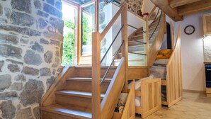 Un escalier en bois, avec un mur de pierre d’un côté et une vue sur la verdure à l’extérieur.