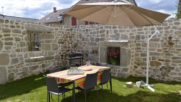A stone-walled outdoor patio with a table and chairs, a large umbrella, and a flower box. - La Maison d'Alphonse 4 people (SAINT LEGER DU MALZIEU)