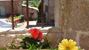 A stone building with a garden in front, featuring red and yellow flowers. - La Maison d'Alphonse 4 people (SAINT LEGER DU MALZIEU)