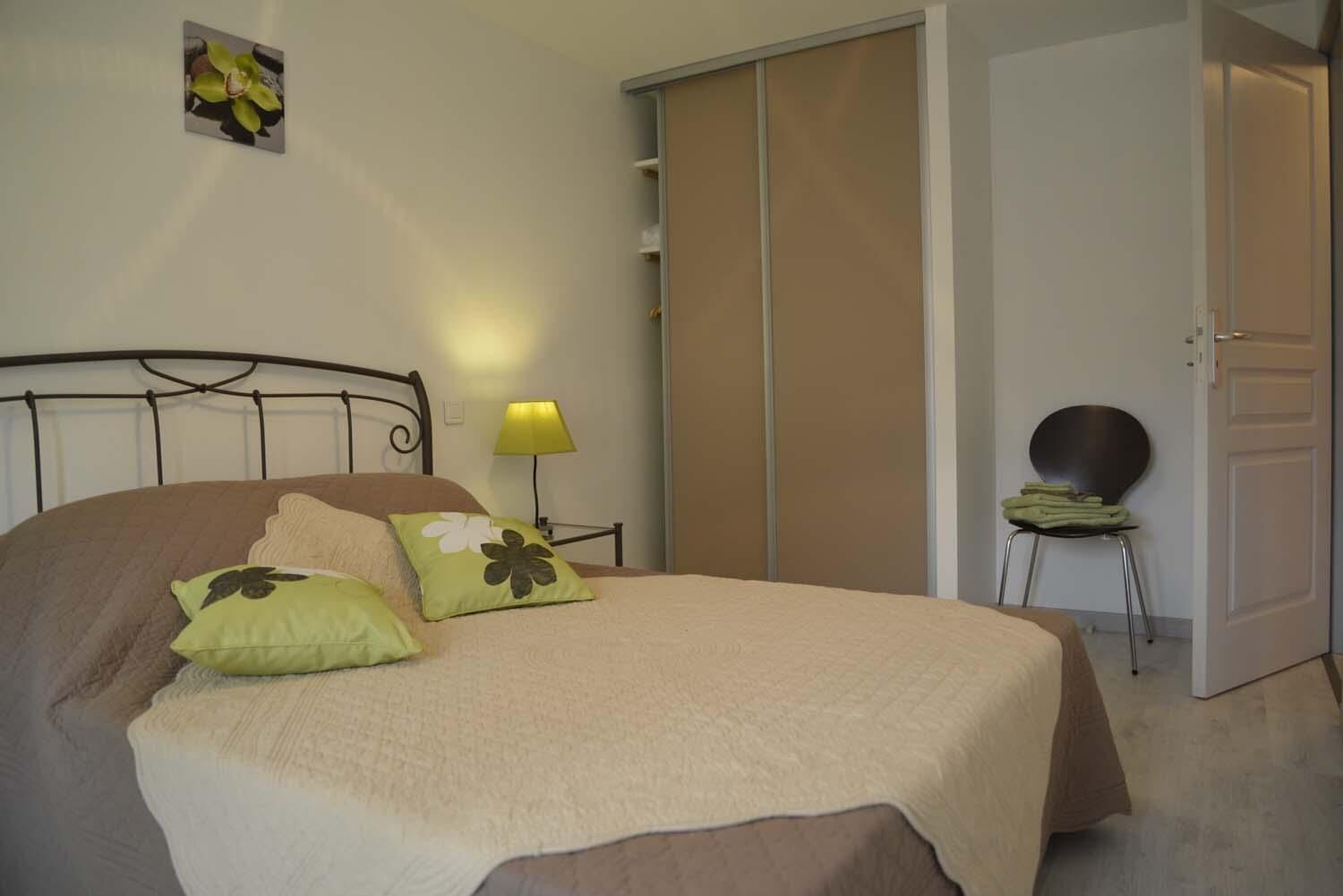 A bedroom with a bed, pillows, a nightstand, a lamp, a chair, and a wardrobe.