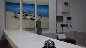 Un mostrador de recepción con un cuadro de barcos en una playa, una cámara de seguridad y un termostato en la pared.
