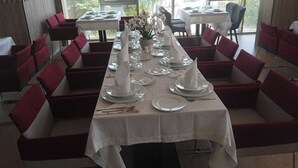 Comedor con una mesa larga dispuesta para una comida, rodeado de sillas con cojines rojos.