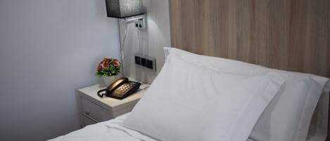 A hotel room with a neatly made bed, a bedside telephone, and a wall-mounted lamp.