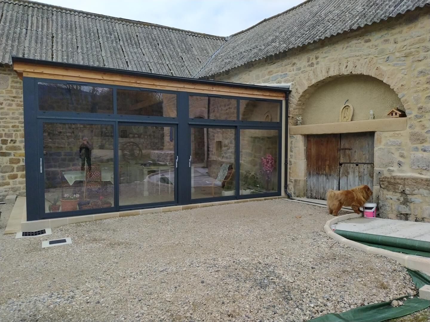 Ein Gebäude aus Stein mit einer großen Glastür und einem kleinen Hund in der Nähe eines pinken Eimers.