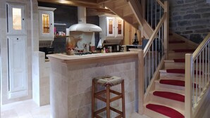 A kitchen with a central island, wooden beams, and a staircase with red steps.