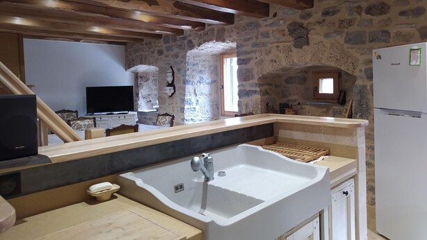 A kitchen with a stone wall, wooden beams, a large sink, and a refrigerator.