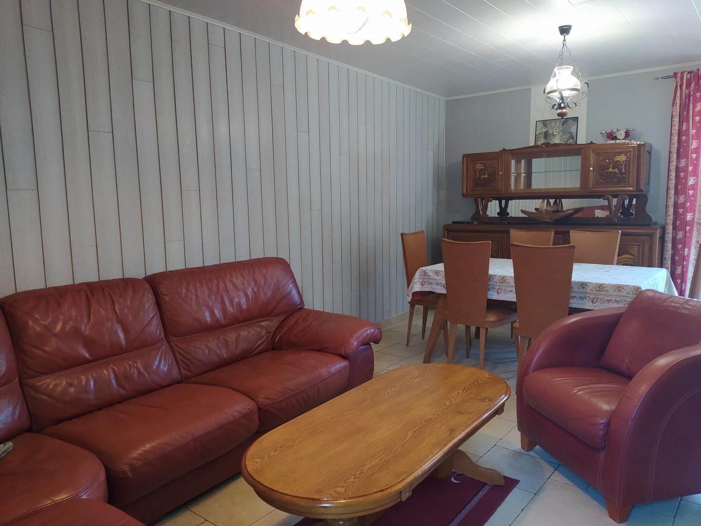 A living room with a brown leather sofa, a wooden coffee table, and a dining area with a table and chairs.
