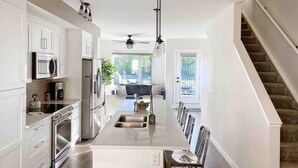 A modern kitchen with white cabinetry, stainless steel appliances, and a central island with a sink. - Modern Mountain Townhouse: private garage/entrance (Canmore)