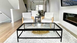 A modern living room with a glass coffee table, two white armchairs, and a fireplace. - Modern Mountain Townhouse: private garage/entrance (Canmore)