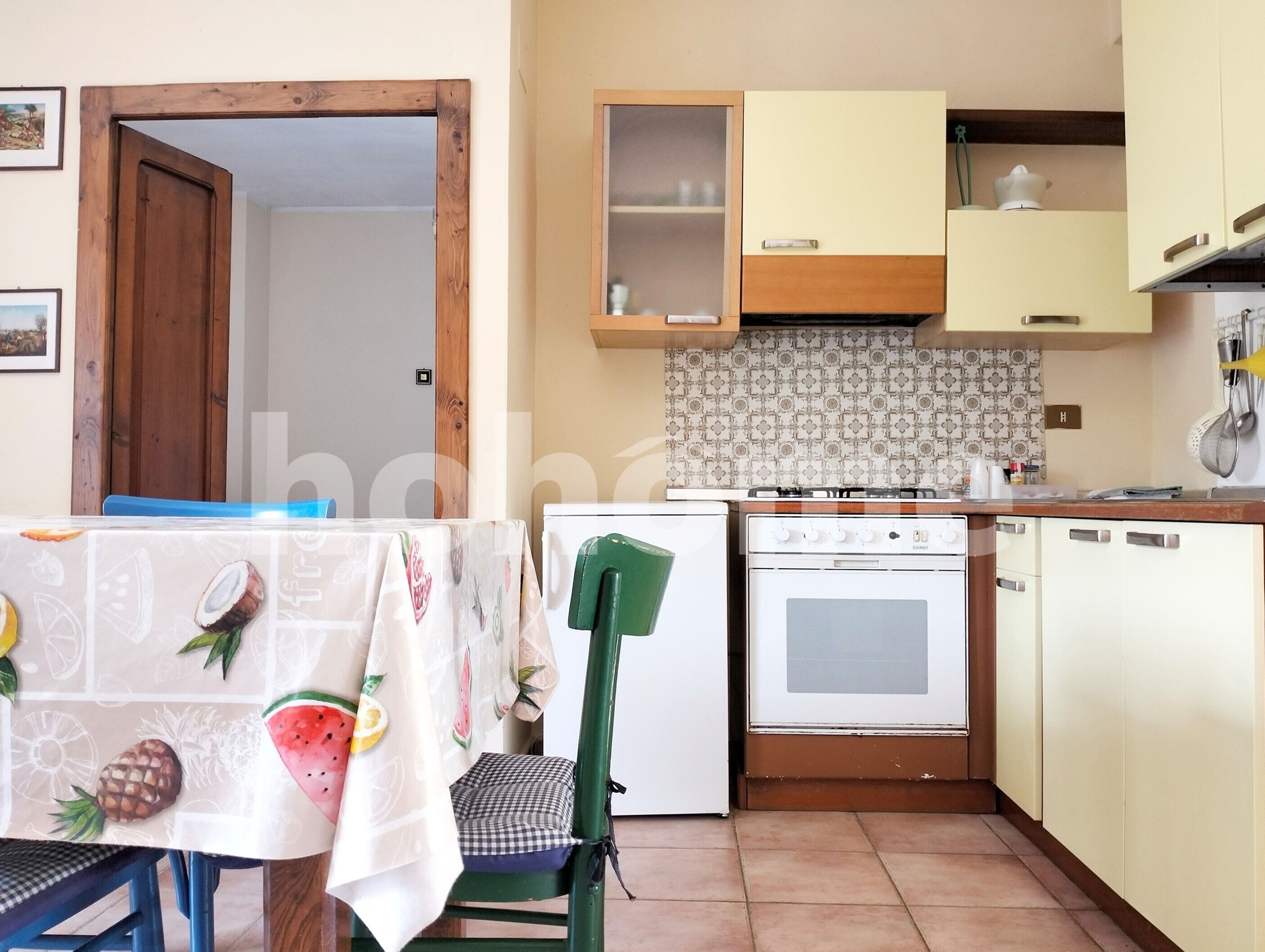 A compact kitchen with a stove, oven, and cabinets. There is a table with a tablecloth and a chair.