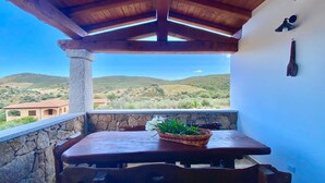 A wooden table with chairs and a basket of flowers on a balcony with a stone wall, overlooking a hilly landscape. - Newly built villas located in a quiet hamlet of San Teodoro.  (Schifoni)