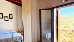 A bedroom with a bed, a mirror, and a view of a stone wall and greenery outside. - Newly built villas located in a quiet hamlet of San Teodoro.  (Schifoni)